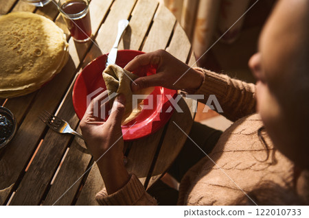 Person rolling a pancake on a red plate in the evening light Person rolling a pancake on a red plate in the evening light 122010733
