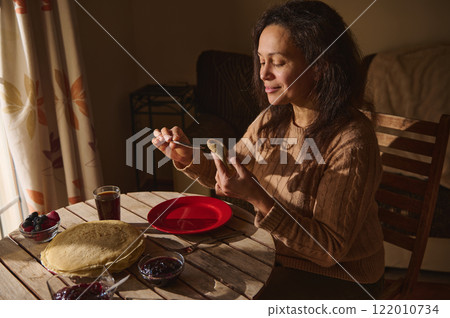 Woman enjoying a cozy breakfast with pancakes and jelly at home Woman enjoying a cozy breakfast with pancakes and jelly at home 122010734
