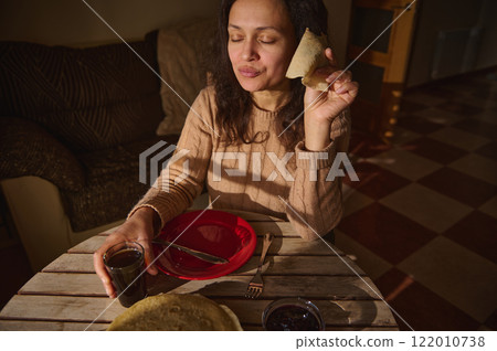 Woman Enjoying Breakfast Crepe with Dark Coffee in Cozy Sunlit Room 122010738