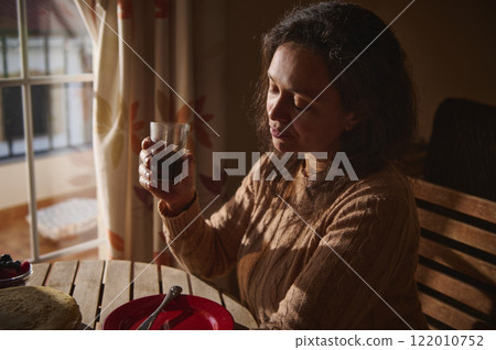 Woman enjoying a beverage by the window in morning light 122010752