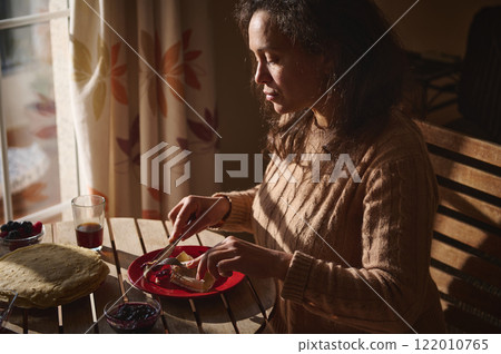 Woman preparing breakfast with crepes and spreads on a sunny morning Woman preparing breakfast with crepes and spreads on a sunny morning 122010765