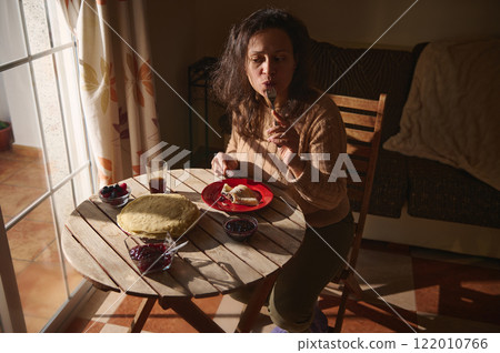 Woman enjoying a warm breakfast at a sunlit table indoors Woman enjoying a warm breakfast at a sunlit table indoors 122010766