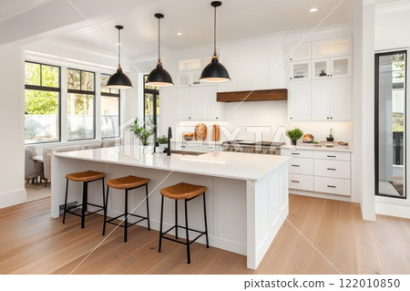 Elegant white kitchen with wooden floor, modern kitchen island and high-end fixtures, open layout with large windows, natural light flooding the space. 122010850