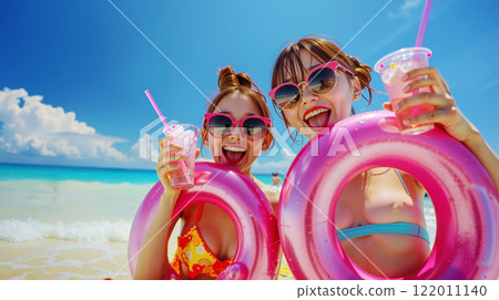 Two young girls in bikinis and sunglasses on the beach with drinks Two young girls in bikinis and sunglasses on the beach with drinks 122011140