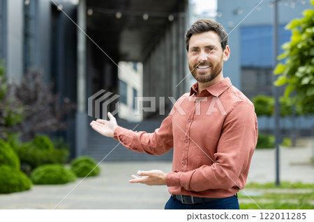 Successful man invites to work in a new team. Businessman looks at the camera and holds hands to the side in a gesture of greeting and invitation. Successful man invites to work in a new team. Businessman looks at the camera and holds hands to the side in a gesture of greeting and invitation. 122011285