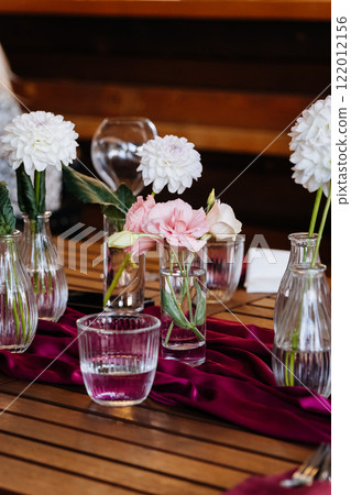 Elegant floral centerpiece arrangement with soft hues and glass vases on a rustic wooden table 122012156