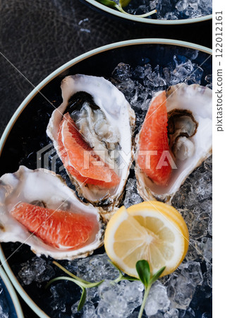 Fresh oysters on ice with grapefruit slices and lemon garnish for a gourmet dining experience Fresh oysters on ice with grapefruit slices and lemon garnish for a gourmet dining experience 122012161