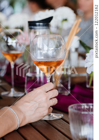 Elegant hand holding a glass of rose wine, surrounded by vibrant table decor at a festive gathering Elegant hand holding a glass of rose wine, surrounded by vibrant table decor at a festive gathering 122012162