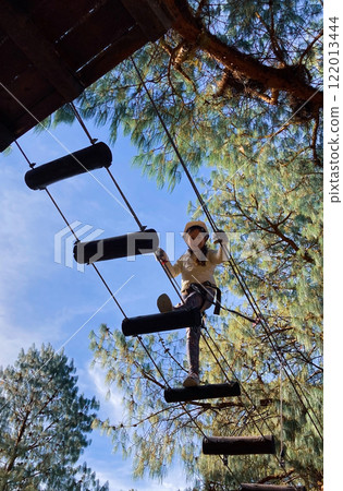 Photo from below of a girl in an adventure park climbing on a rope course Photo from below of a girl in an adventure park climbing on a rope course 122013444