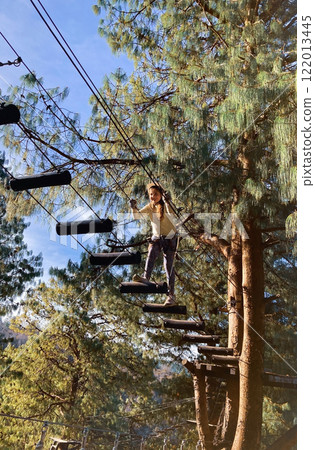 Girl in forest adventure park. wearing helmet climbing a high ropes course. Girl in forest adventure park. wearing helmet climbing a high ropes course. 122013445