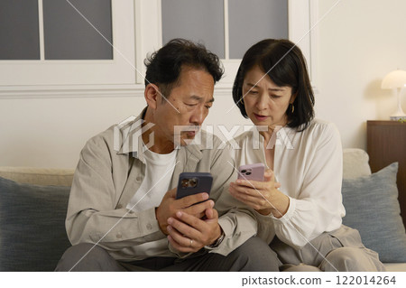 一對中年夫婦晚上在客廳一邊使用智慧型手機一邊擔心 122014264