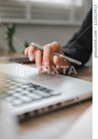 A hand using a laptop touchpad with a pen, symbolizing modern business and productivity in an office environment. A hand using a laptop touchpad with a pen, symbolizing modern business and productivity in an office environment. 122015413
