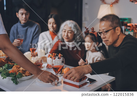 Multi-Generation Family Celebrate Christmas At Home Wearing Santa Hats And Antlers Opening Presents 122015836