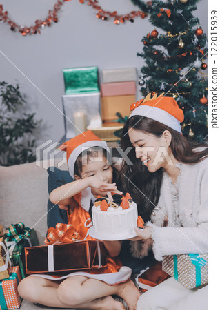 Merry Christmas and Happy Holidays. Cheerful mom and her cute daughter girl exchanging gifts. Parent and little child having fun near tree indoors. 122015939