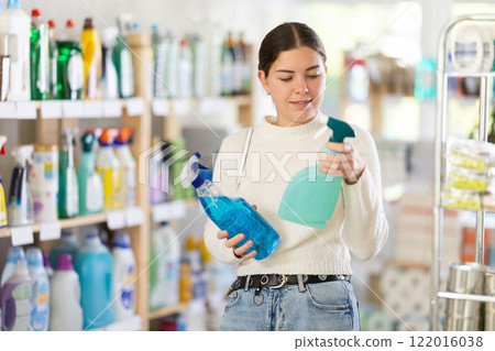 Girl housewife in household store examines package, chooses household chemical spray Girl housewife in household store examines package, chooses household chemical spray 122016038