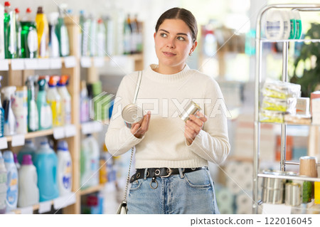Girl housewife in household store examines package, chooses tin can Girl housewife in household store examines package, chooses tin can 122016045