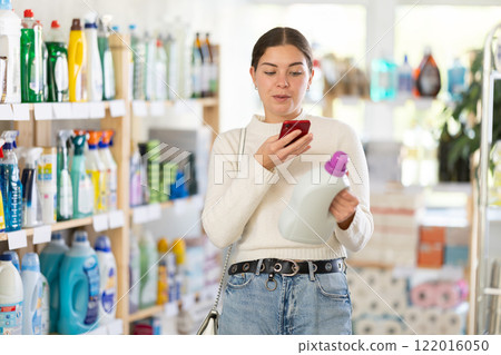 Before making purchase, young woman buyer scans QR code on packaging of liquid detergent Before making purchase, young woman buyer scans QR code on packaging of liquid detergent 122016050