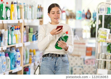 Before making purchase, young woman buyer scans QR code on packaging of dishwashing detergent 122016063
