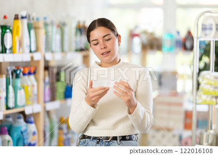 Girl housewife in household store examines package, chooses products toothpaste and related products 122016108