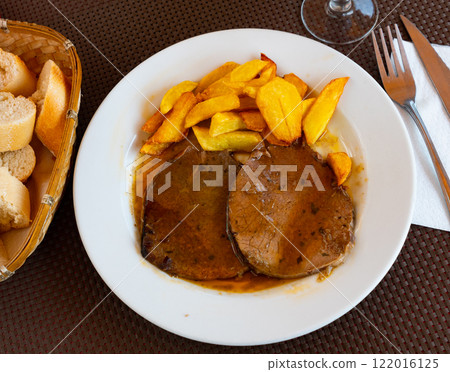 Tasty baked beef steak in fragrant gravy served with potatoes and pepper at plate. Traditional Spanish dish 122016125