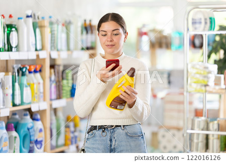 Before making purchase, girl buyer scan QR code on packaging of polishing agent for wooden furniture Before making purchase, girl buyer scan QR code on packaging of polishing agent for wooden furniture 122016126