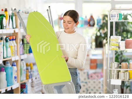 Girl housewife in household store examines goods, chooses ironing board 122016128