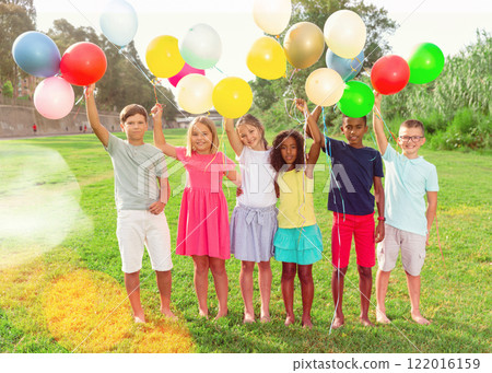 Happy tweens with balloons on green meadow in summer park Happy tweens with balloons on green meadow in summer park 122016159