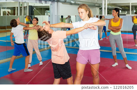 Kids in pair exercising self-defense movements during group class with female coach Kids in pair exercising self-defense movements during group class with female coach 122016205