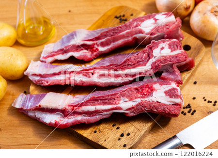 Raw beef ribs on board, potato tubers and whole onions 122016224