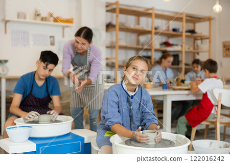 Children working at potter's wheel with teacher in art studio Children working at potter's wheel with teacher in art studio 122016242