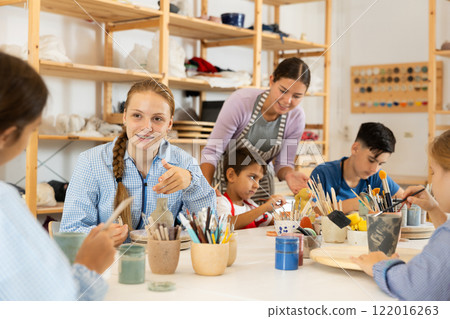 Children painting ceramics with a teacher 122016263