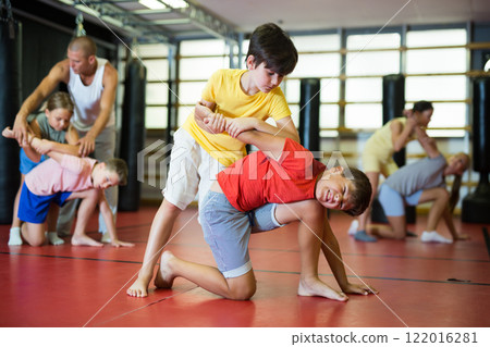 Boys and girls in gym exercising armlock move Boys and girls in gym exercising armlock move 122016281