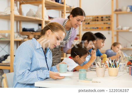 Girl paints ceramic dishes 122016287