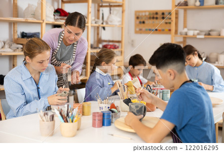 Children paint ceramic work-pieces at table with teacher in art studio Children paint ceramic work-pieces at table with teacher in art studio 122016295