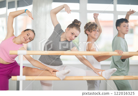 Two teenage girls practicing leg stretching exercise during ballet classes 122016325