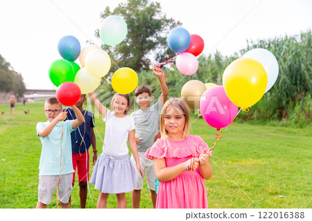 Cheerful blonde tween girl with balloons in hands in city park Cheerful blonde tween girl with balloons in hands in city park 122016388
