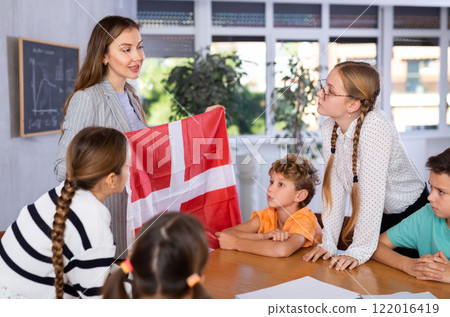 School teacher tells students about Denmark and holds a Denmark flag in hands. School teacher tells students about Denmark and holds a Denmark flag in hands. 122016419