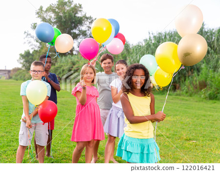 Smiling african american preteen girl with balloons on green lawn with friends Smiling african american preteen girl with balloons on green lawn with friends 122016421