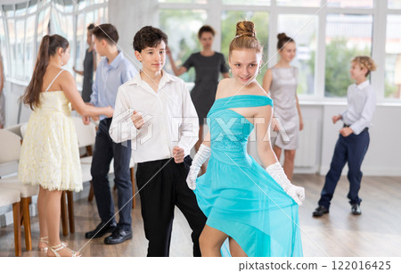 Teen girl in elegant evening dress dances incendiary twist with boy partner during choreography lesson 122016425