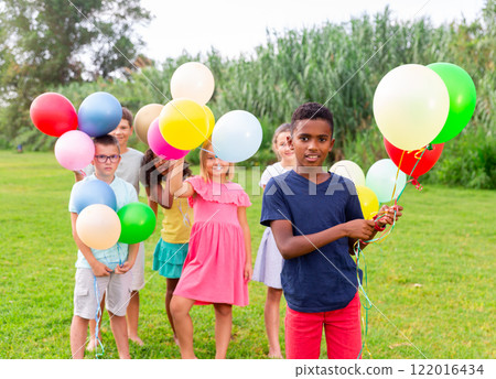 Happy african american preteen boy with balloons on lawn with friends Happy african american preteen boy with balloons on lawn with friends 122016434