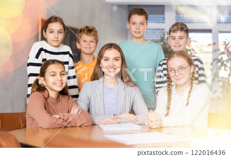 Group portrait of excited tween schoolchildren around positive young female teacher in classroom Group portrait of excited tween schoolchildren around positive young female teacher in classroom 122016436