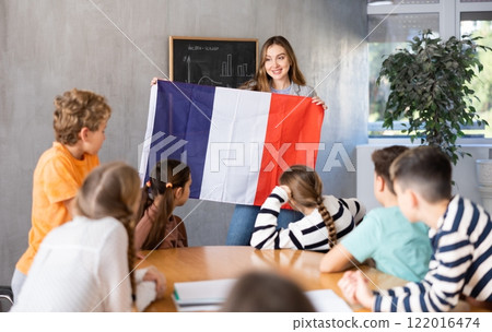 Joyful female teacher discussing with preteens students state flag of France in auditory of middle school Joyful female teacher discussing with preteens students state flag of France in auditory of middle school 122016474