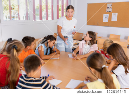 Kids sitting around desk in classroom and studying during lesson 122016545