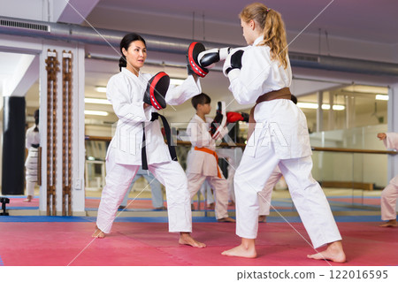 Female trainer in boxing gloves conducts sparring and teaches punches to girl in karate and self-defense training Female trainer in boxing gloves conducts sparring and teaches punches to girl in karate and self-defense training 122016595