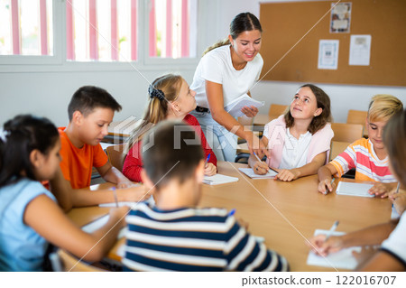 Female teacher conducting lesson with preteen children sitting around desk 122016707