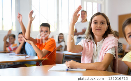 Diligent tween schoolgirl raising hand during lesson in classroom Diligent tween schoolgirl raising hand during lesson in classroom 122016713