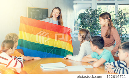 Young female teacher showing flag of LGBT to schoolchildren preteens and explaining LGBTQ social movements in classroom Young female teacher showing flag of LGBT to schoolchildren preteens and explaining LGBTQ social movements in classroom 122016721