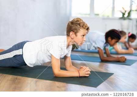 In sport studio with group of friends, boy perform plank pose asana 122016728