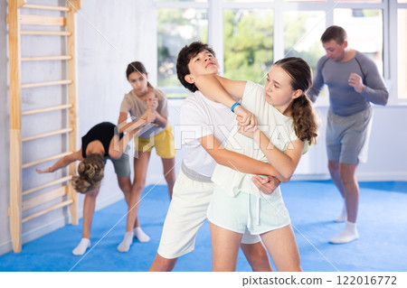 Preteen children, boy and girl, working in pair mastering new self defense moves at gym 122016772
