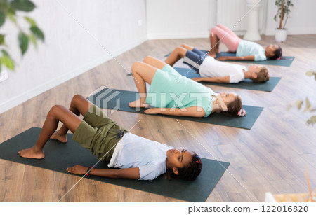 Girls and boys doing abdominal crunches with outstretched arms to strengthen abs and core muscles during group yoga class in studio 122016820